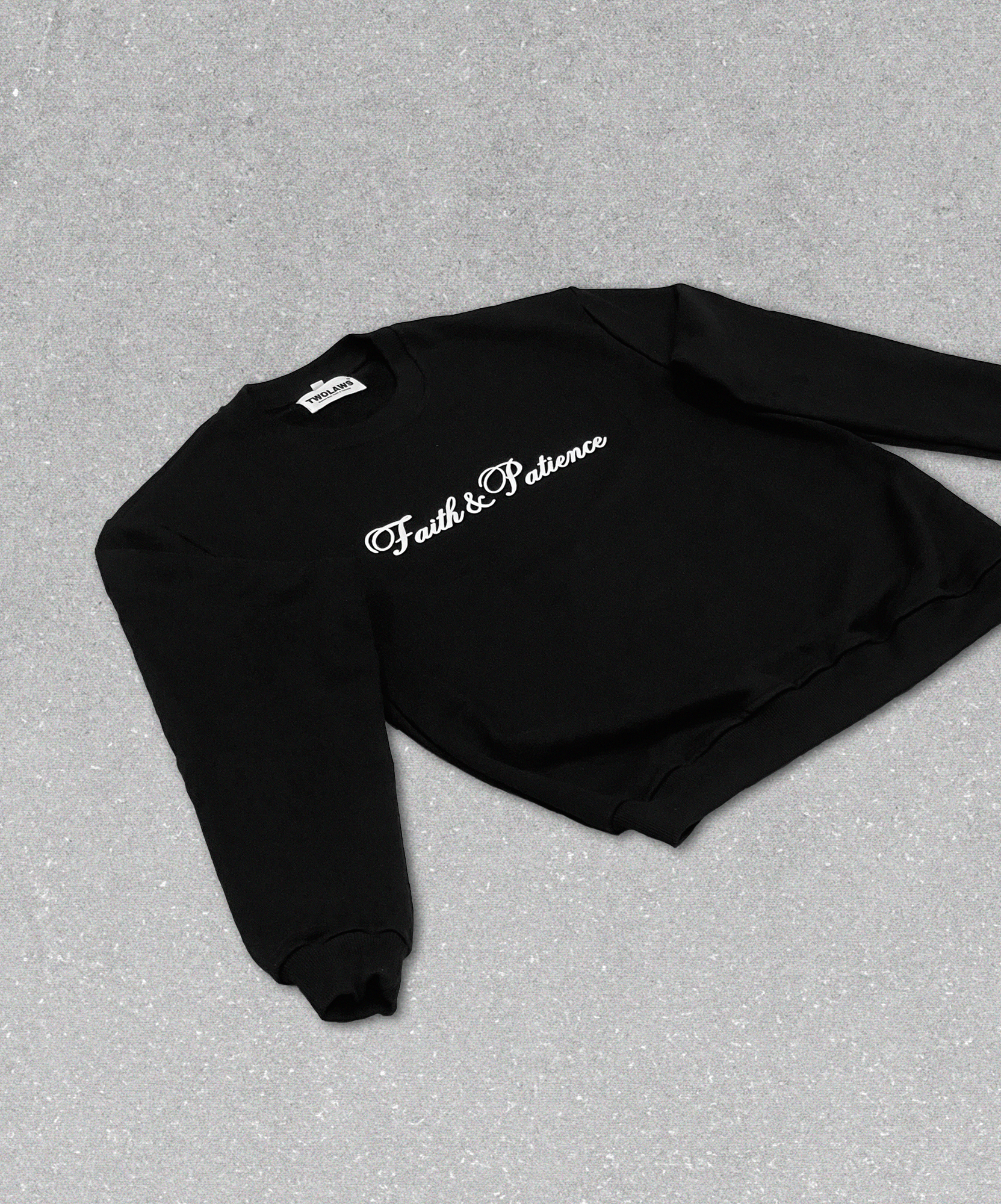 Oversized black streetwear sweatshirt with 'Faith & Patience' printed on front and TWOLAWS logo on back, laid flat on the floor.