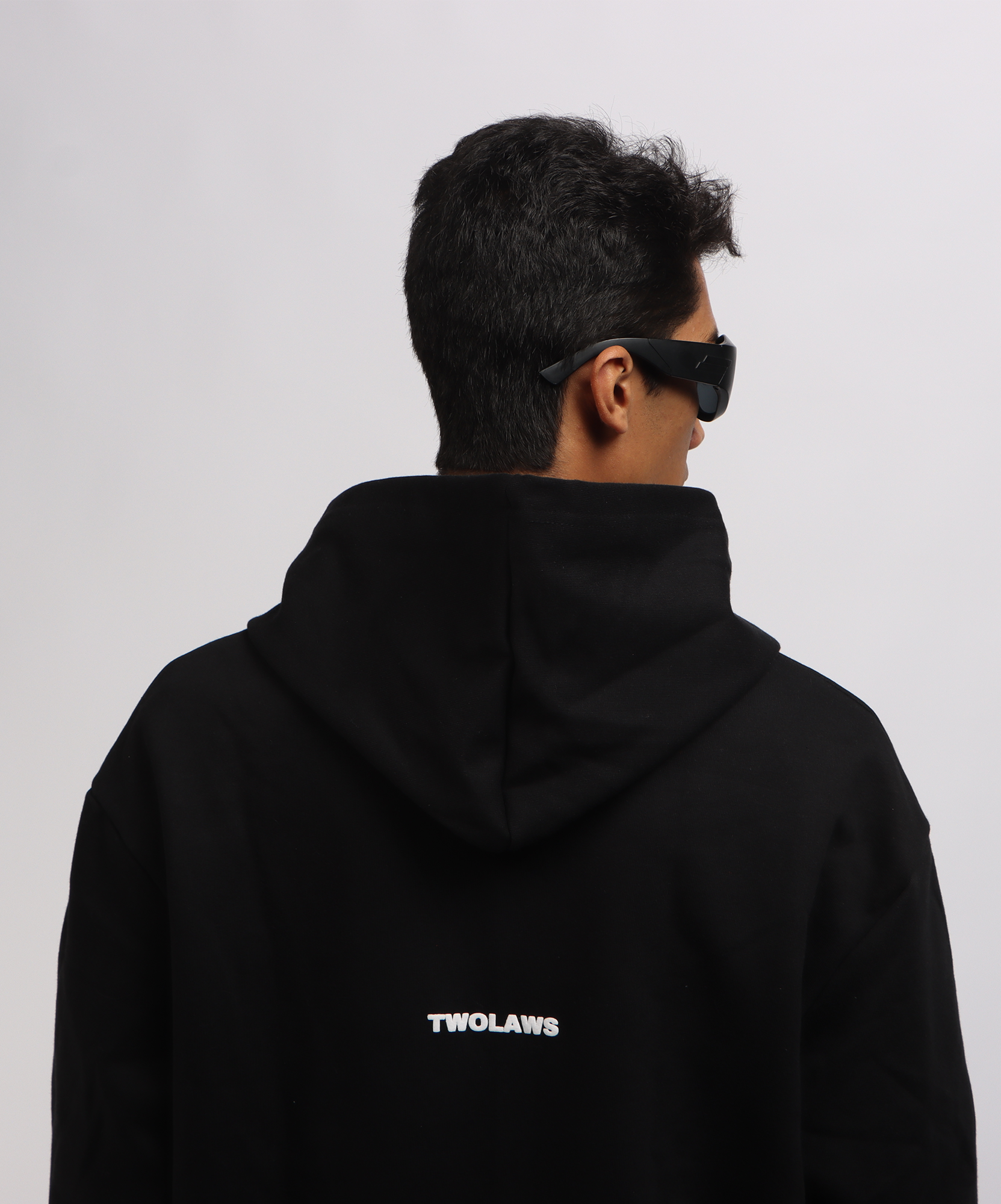 Close-up of model wearing TWOLAWS Black Hoodie featuring bold TWOLAWS text on the back and oversized fit.